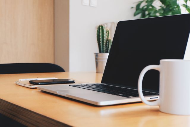 new or ex UK laptop placed on a tidy office desk between mug and phone placed on notepad