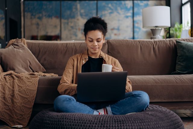 woman using laptop with a cup in hand in a relaxed indoor setting