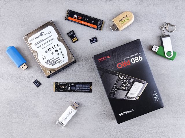 A flat lay of various computer data storage devices including hard disk, flash disk, memory card, etc. on a grey surface